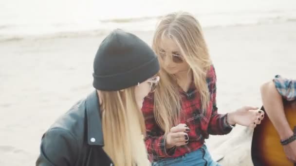 A young guy playing guitar sitting on a log, two attractive blond women clap their hands and laugh close-up. — Stock Video