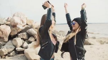 İki çekici sarışının atlama ve plaj yakın çekim yavaş hareket üzerinde kayalar arka plan karşı çıkıyor.