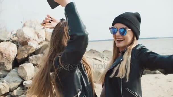 Twee jonge blonde meisjes in lederen jassen dansen op het strand close-up slow motion. — Stockvideo