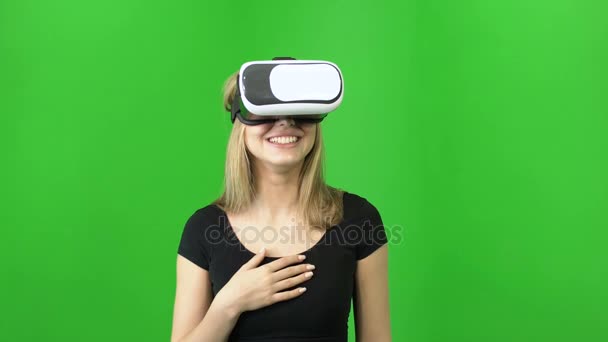 20-летняя привлекательная девушка смеется во время ношения в VR очки шлем на зеленом фоне хромы ключевой — стоковое видео