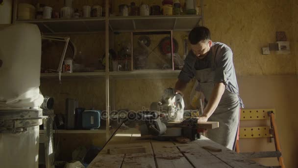 Trabajador de madera barbudo en trabajo de delantal con máquina de carpintería en el taller con retroiluminación — Vídeos de Stock