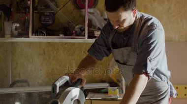 Portre konsantre 20s woodworker daire testere kullanarak önlük sakallı. Testere ahşap tahta arka plan üzerinde talaş ile eller