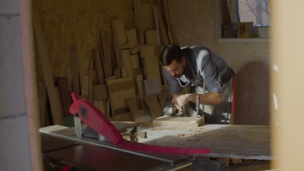 20'li yaşlarda woodworker işleri brashing makine ile güneşli gün atölyede sakallı — Stok video