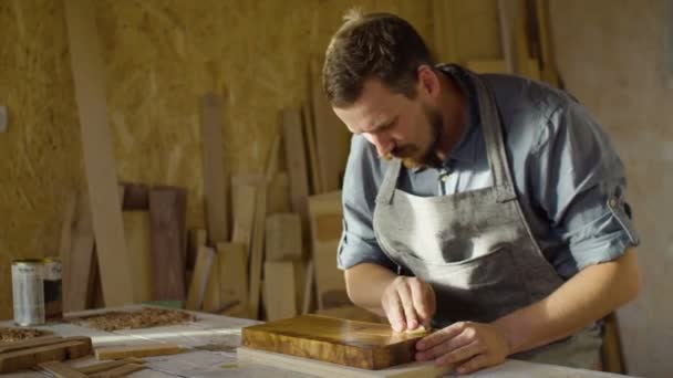 Портрет бородатого столяра 20-х годов массирует лак в деревянной доске в мастерской — стоковое видео