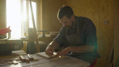20'li yaşlarda marangoz woodworker arka ışık güneş fişekleri ile ahşap tahta üzerinde çizim önlük sakallı