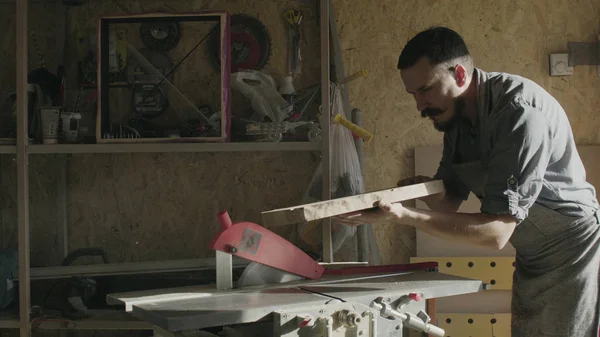 Trabajador de madera barbudo en trabajo de delantal con máquina de carpintería en el taller con retroiluminación — Foto de Stock