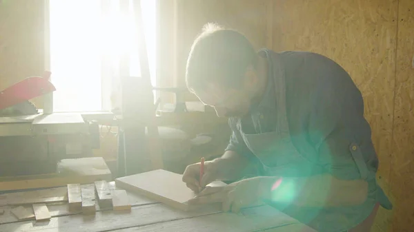 20'li yaşlarda adam marangoz ahşap tahta üzerinde çizim sakallı. güneşli bir günde atölye