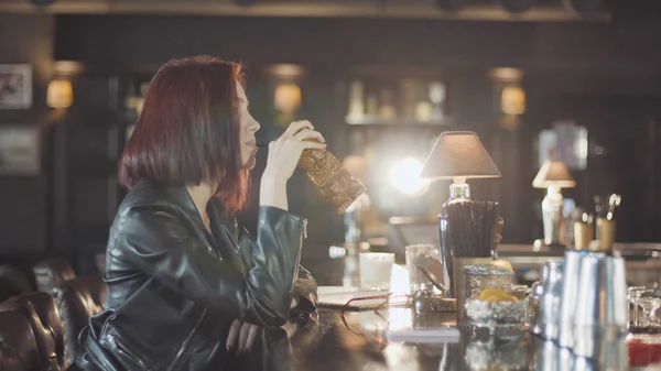20'li seksi güzellik Kızıl saçlı kadın siyah deri ceketli mi içki kokteyl, kamera ve flört gülümsüyor bardaki bakarak
