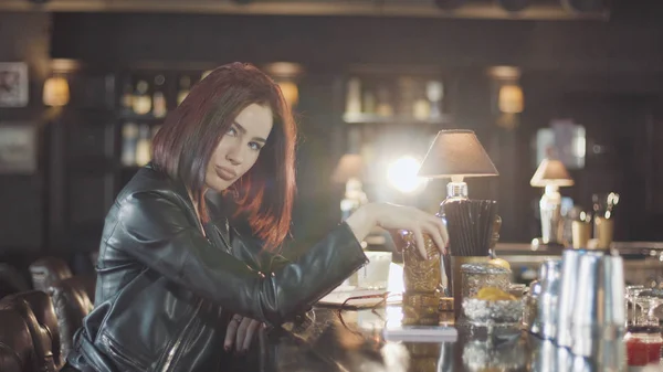 20'li seksi güzellik Kızıl saçlı kadın siyah deri ceketli mi içki kokteyl, kamera ve flört gülümsüyor bardaki bakarak