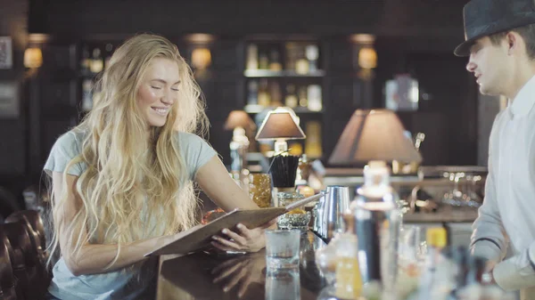 Barman pomáhá žena blond 20s učinit volbu v menu bar — Stock fotografie
