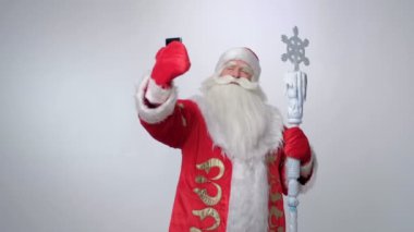 Neşeli Rus Noel Baba akıllı telefonuyla selfie çekiyor ve gülümsüyor.