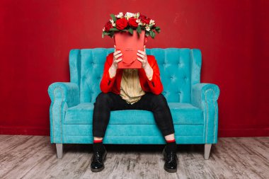 Adam mavi kanepede elinde bir kutu kırmızı gülle bekliyor.