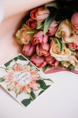 Bir buket pembe ve şeftali çiçekli tebrik kartı.