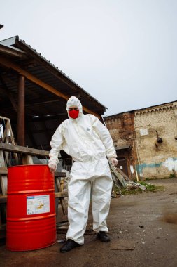 Korumalı takım elbiseli adam, kırmızı tıbbi maske ve lateks eldivenler. Şehrin harabelerinde Coronavirus COVID-19 salgını sırasında.