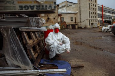 Korumalı takım elbiseli adam, kırmızı tıbbi maske ve lateks eldivenler. Şehrin harabelerinde Coronavirus COVID-19 salgını sırasında.
