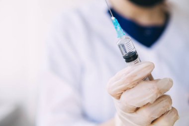 Genç doktor elinde elinde ilaç ve koronavirüsle tıbbi şırınga tutuyor.