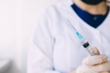 Genç doktor elinde elinde ilaç ve koronavirüsle tıbbi şırınga tutuyor.