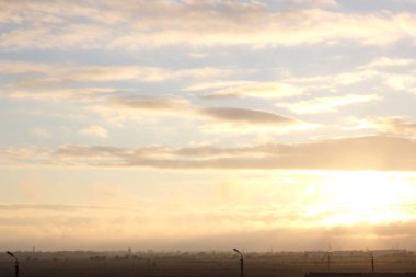 Yaz günbatımında yeşil bir alanın üzerinde hafif bir sis, gökyüzündeki renklerin eğimi, bulutlu hava, uzaktaki ağaçların siluetleri, arka planda odaklanma, keskinlik ve bulanıklık, bokeh, doku, turuncu, pembe, mavi