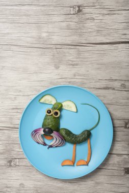 Mavi tabakta ve ahşap masada vurulan eğlenceli sebze köpeği.