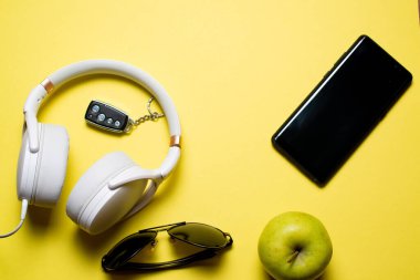 Kulaklık, güneş gözlüğü, elma, telefon sarı arka planda.