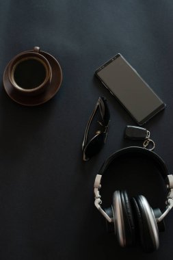 Bir fincan kahve, güneş gözlüğü, akıllı telefon, siyah arka planda kulaklık.