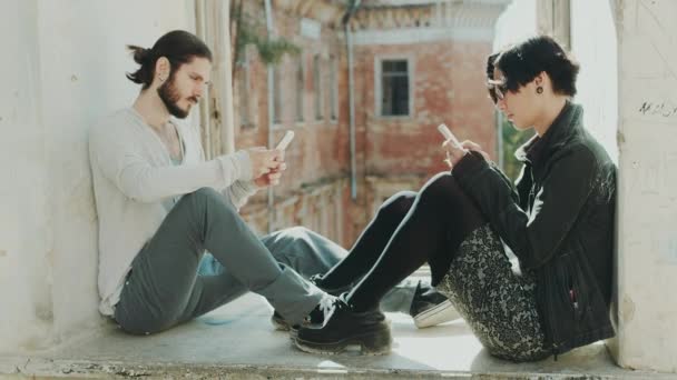 Jovem casal hipster sentado na janela, usar telefones celulares. Conceito - a falta de comunicação ao vivo, problemas de relacionamento — Vídeo de Stock