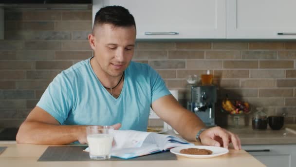 Un jeune homme lisant un livre dans la cuisine, debout à côté d'un verre de lait. Une alimentation et un mode de vie sains — Video
