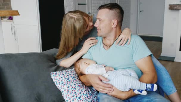 Jovem mulher carinhosamente abraçando seu marido que está segurando em suas mãos filho de dois meses — Vídeo de Stock
