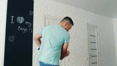 Mutlu genç baba iki ay oğluyla oynuyor. Onu okşuyor, gülümsüyor. Aile konforu ve ebeveynlerin bakımı