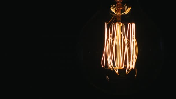 Old light bulb lights up continuously. On a black background, slightly swaying — Stock Video