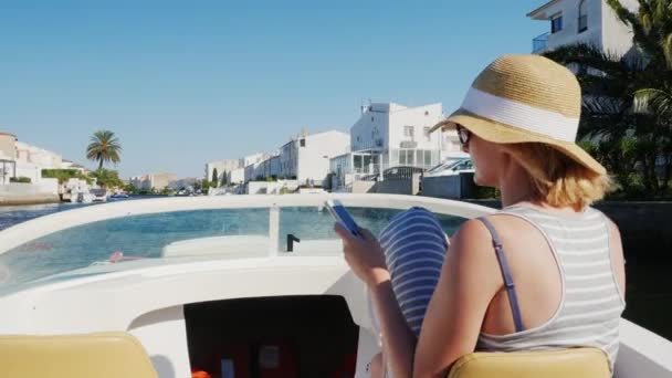Empuriabrava, España: Joven turista con sombrero flotando en un barco sobre el canal, utilizando un teléfono móvil. Concepto - Vacaciones en Europa — Vídeos de Stock
