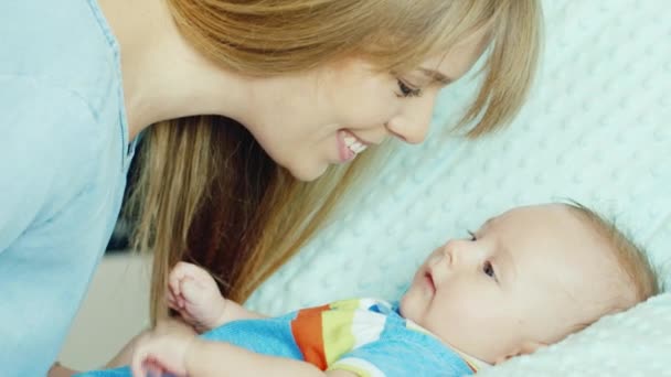 Glückliche junge Mutter lächelt zu seinem Sohn zwei Monate. Das Baby liegt in der Krippe — Stockvideo
