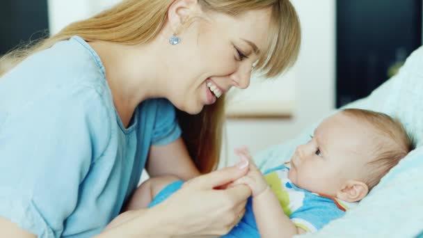 Feliz madre joven mirando a su hijo, sosteniendo su pluma. El bebé yace en la cuna. — Vídeos de Stock