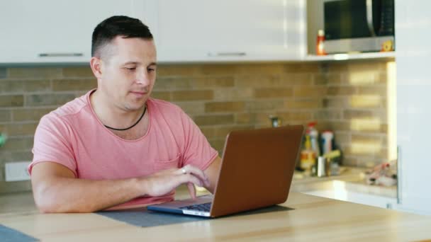Young attractive man working with laptop at the kitchen — Stock Video
