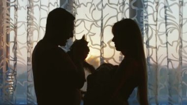 Çocuklu ve köpekli mutlu bir aile. Pencerede dururken, babam elinde bir köpek tutar, annem bebeği emzirir..
