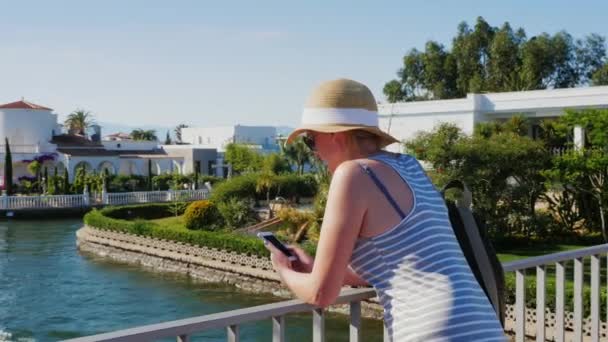 Toerist met de telefoon. Staande op de brug over het kanaal in Empuriabrava, Spanje. Het concept-een reis naar Europa, altijd verbonden — Stockvideo