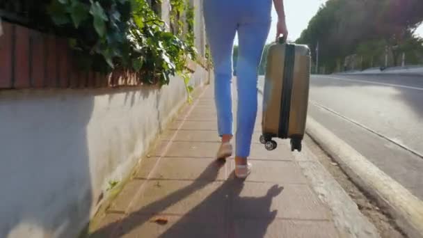 Steadicam shot: Женщина-туристка, идущая по дороге с дорожной сумкой. Испания курорт. Вид сзади — стоковое видео