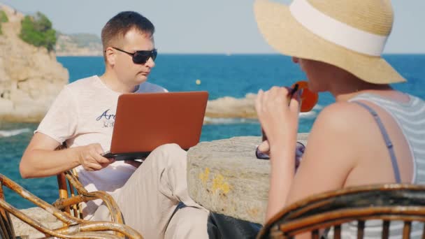 Das Paar im Resort. Frau trinkt Cocktail, Mann arbeitet mit Laptop — Stockvideo