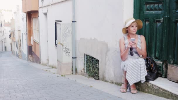Turisztikai nő használ smartphone. Ő ül a küszöbön, a régi ház a város. Koncepció - problémák utazó — Stock videók