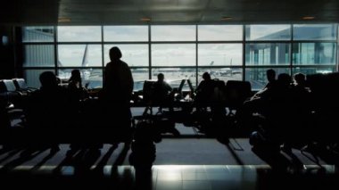 İnsanlar güneşli bir günde terminal havaalanında uçuş için bekliyor. Pencerenin dışında uçak çıkartıyor. Bir insan, hiçbir tanınabilir yüzler siluetleri görebilirsiniz