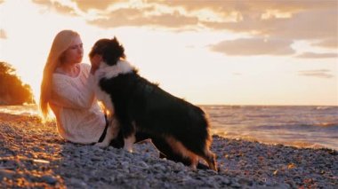 Köpeğimi seviyorum. Sarışın genç kadın laskat sobbaku onu, onu öpüyor. Gün batımında göl kenarında oturmak
