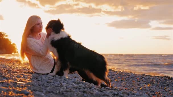 Αγαπώ τον σκύλο μου. Νεαρή ξανθιά γυναίκα laskat sobbaku της, φιλά. Καθίστε από τη λίμνη στο ηλιοβασίλεμα — Αρχείο Βίντεο