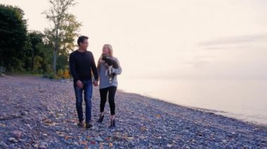 Genç erkek ve kadın gün batımında sahilde yürüyüş. Bir kadın elinde bir köpek yavrusu taşır