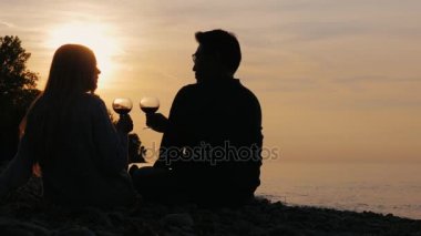 Romantik çok etnik gruptan oluşan çift plaj veya göl üzerinde şarap içme. Bir gün batımında arkasında onların siluetleri görebilirsiniz. Asyalı erkek ve beyaz kadın