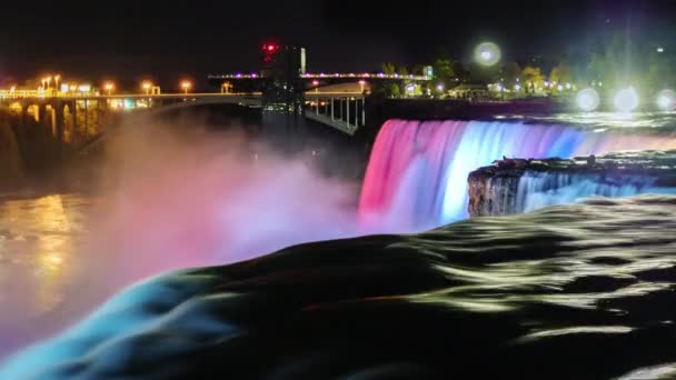 Niagara Falls in de nacht. De jets van vallende water zijn verlicht met gekleurde schijnwerpers. De stroom van het water op een donkere voorgrond — Stockvideo