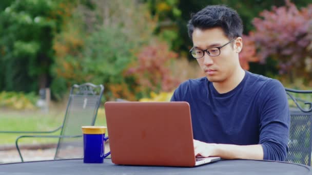 Koreanische Programmierer arbeitet mit einem Laptop auf der Straße oder in einem Café. In der Nähe steht eine Tasse Kaffee — Stockvideo