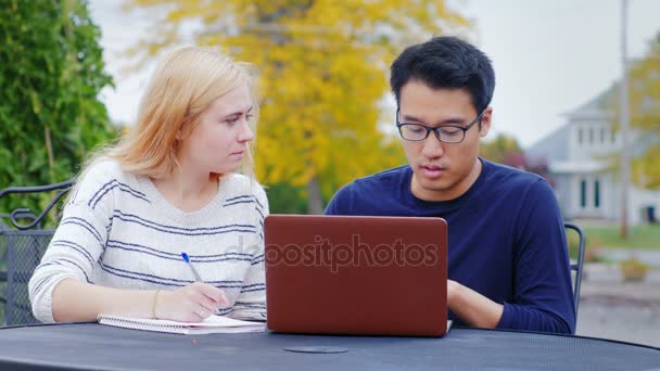 Twee zakenman - Aziatische man en Kaukasische vrouw communiceren, werken met een laptop. Het zomerterras — Stockvideo