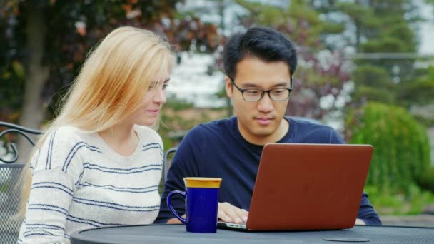 Multiethnische Teams, die zusammenarbeiten. asiatischer Mann und kaukasische Frau, die mit einem Laptop arbeiten. auf der Sommerterrasse oder im Café — Stockvideo