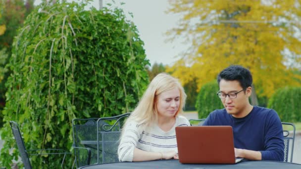 Young friends - Asian man and Caucasian woman talking on the terrace, enjoying the laptop — Stock Video