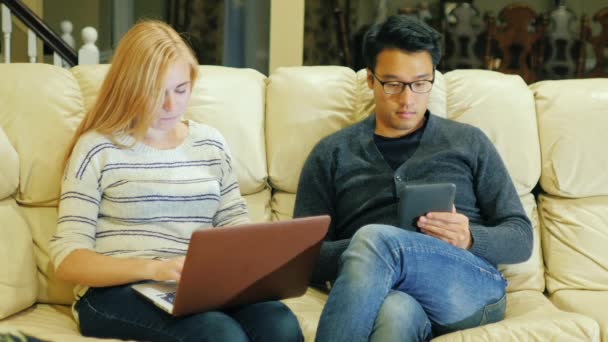 Kaukasierin mit Laptop. Naher asiatischer Mann mit einem E-Book. Zeit gemeinsam zu Hause verbringen — Stockvideo